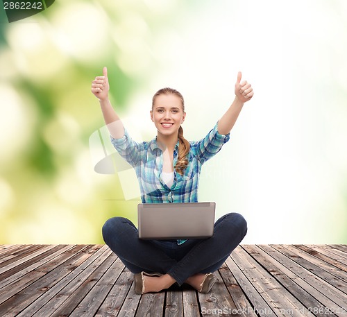 Image of smiling woman with laptop and showing thumbs up