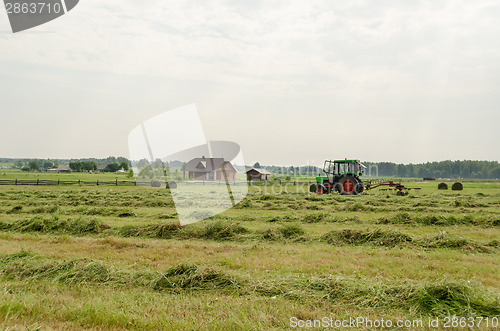 Image of tractor turning raking cut hay in field 