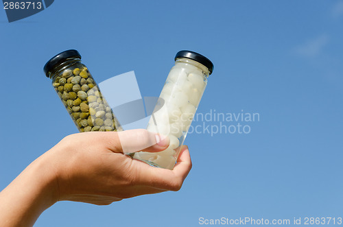 Image of hand hold caper garlic jar on blue sky background 