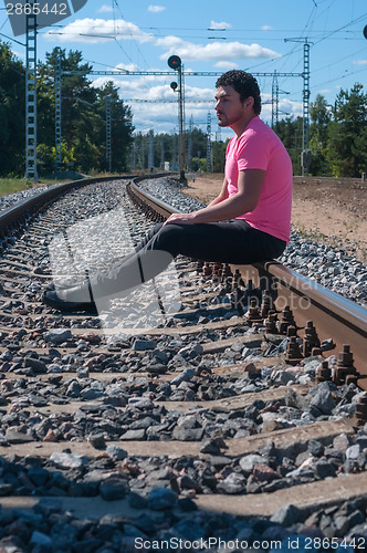 Image of Single man in pink t-shirt sitting on train tracks