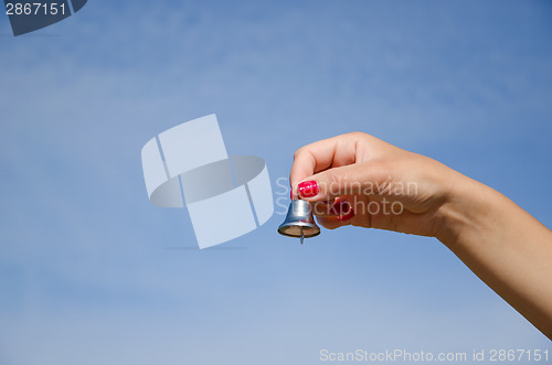 Image of hand hold jingle silver bell on blue sky 
