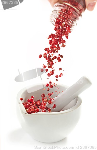 Image of red peppercorns falling into mortar and pestle