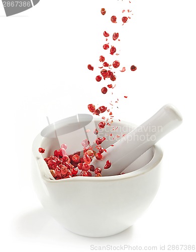 Image of red peppercorns falling into mortar and pestle