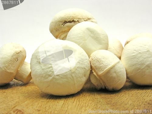 Image of White  mushrooms on a brown wooden plate