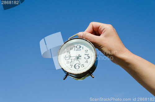 Image of hand hold clock with big numeral on sky background 