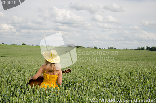 Image of Country woman in dress play guitar wheat field 