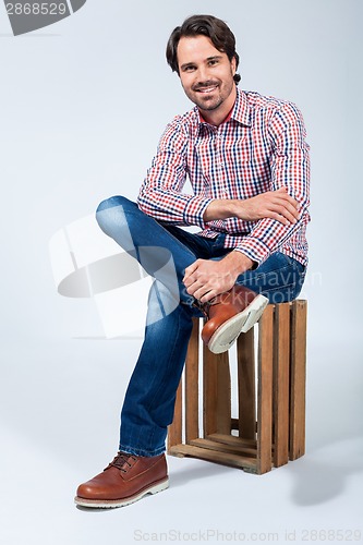 Image of Handsome young man sitting on a wooden box