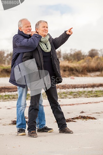 Image of happy elderly senior couple walking on beach