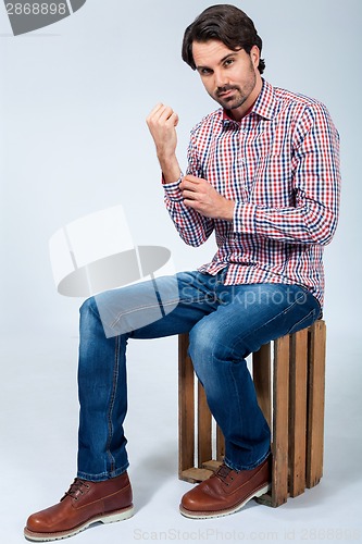 Image of Handsome young man sitting on a wooden box