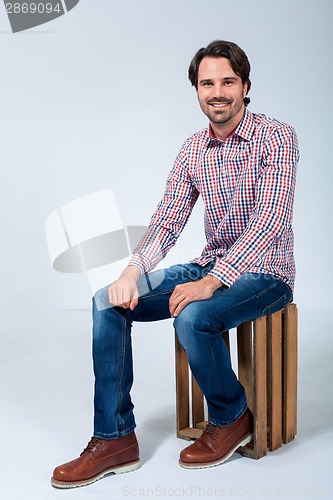 Image of Handsome young man sitting on a wooden box