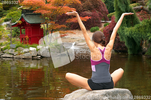 Image of Woman Reaches for the Sky on Rock in Yoga Pond
