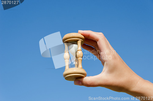 Image of hand hold wooden hourglass on blue sky background 