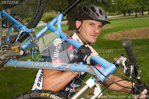 Image of Serious Male Bicycle Racer Carrying Bike During Iron Man Triathl