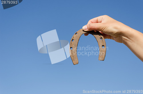 Image of rusty iron horseshoe in hand on blue sky bckground 