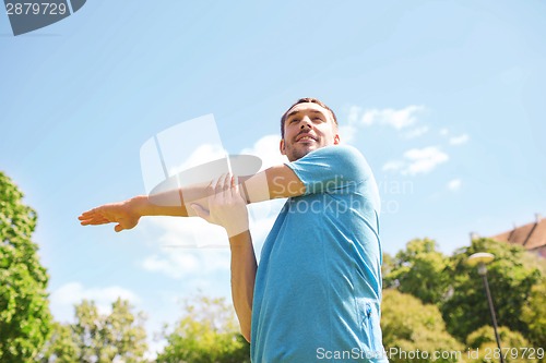 Image of smiling man stretching outdoors
