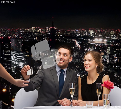 Image of smiling couple paying for dinner with credit card