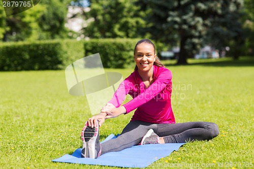 Image of smiling woman stretching leg on mat outdoors