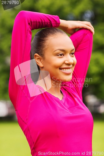 Image of smiling black woman stretching leg outdoors