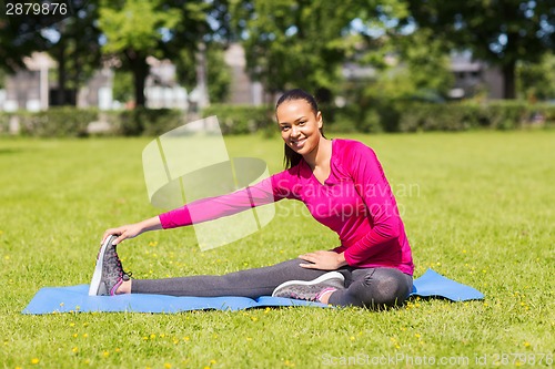 Image of smiling woman stretching leg on mat outdoors