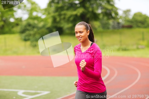 Image of smiling young woman running on track outdoors