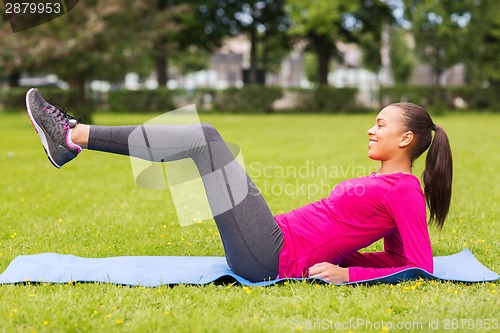 Image of smiling woman doing exercises on mat outdoors