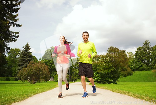 Image of smiling couple with earphones running outdoors