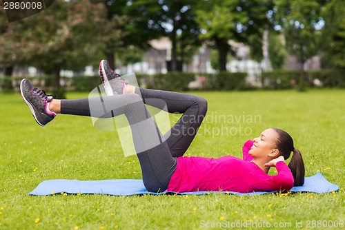 Image of smiling woman doing exercises on mat outdoors