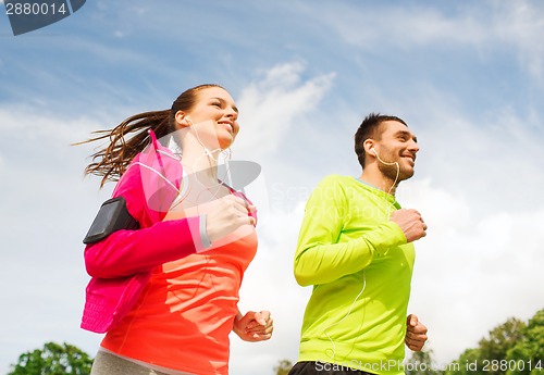 Image of smiling couple with earphones running outdoors