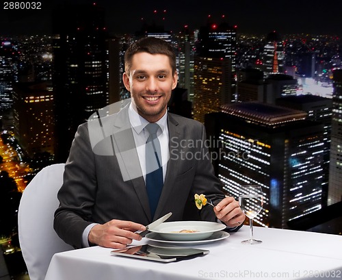 Image of smiling man with tablet pc eating main course