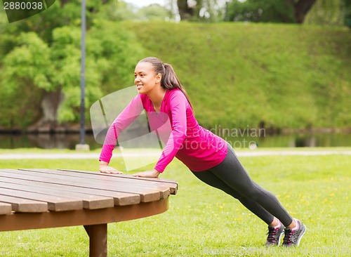 Image of smiling woman doing push-ups on bench outdoors