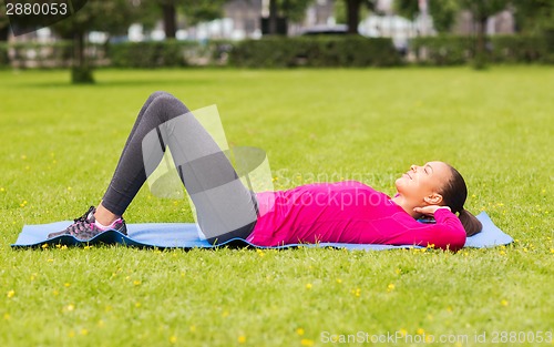 Image of smiling woman doing exercises on mat outdoors