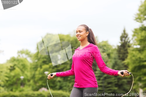 Image of smiling woman exercising with jump-rope outdoors