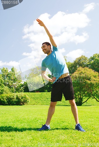 Image of smiling man stretching outdoors