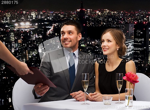 Image of waiter giving menu to happy couple at restaurant