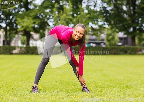 Image of smiling black woman stretching leg outdoors