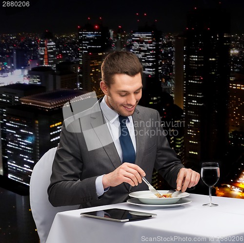 Image of smiling man with tablet pc eating main course