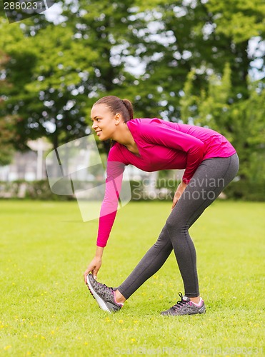 Image of smiling black woman stretching leg outdoors