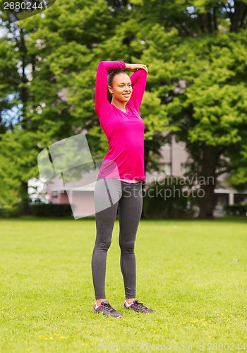 Image of smiling black woman stretching leg outdoors