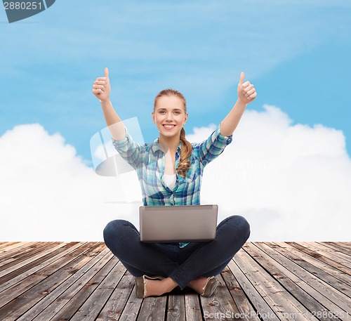 Image of smiling woman with laptop and showing thumbs up