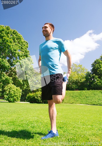 Image of smiling man stretching outdoors