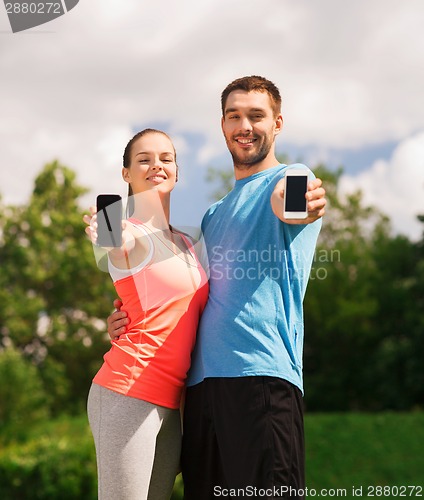 Image of two smiling people with smartphones outdoors