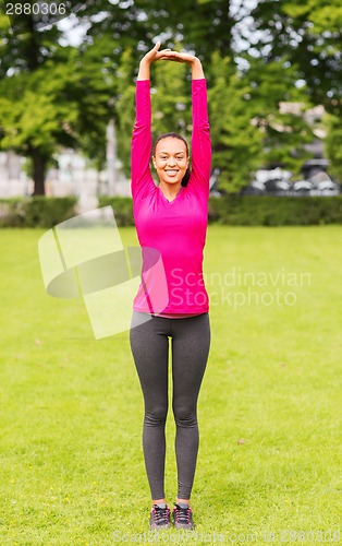 Image of smiling black woman stretching leg outdoors