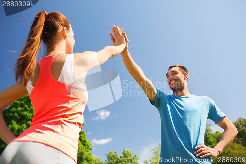 Image of two smiling people making high five outdoors
