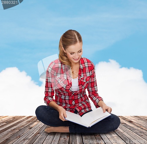 Image of smiling young woman sitting on floor with book