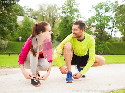 Image of smiling couple tying shoelaces outdoors