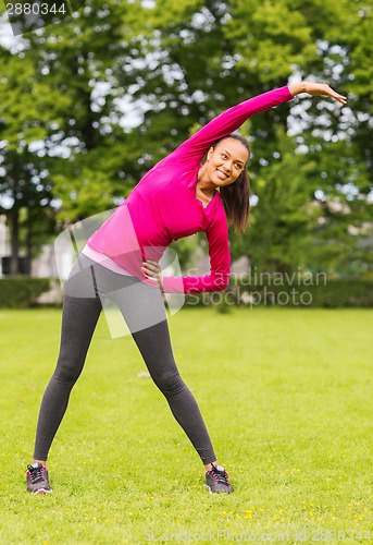 Image of smiling black woman stretching leg outdoors