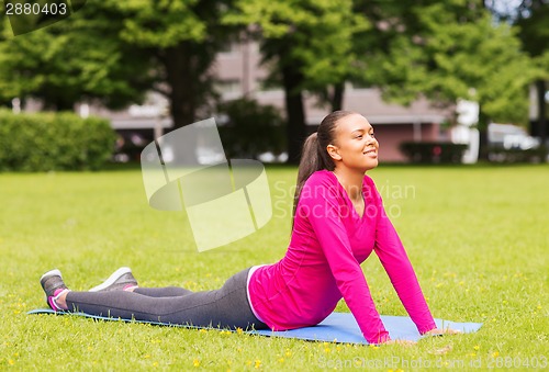 Image of smiling woman stretching on mat outdoors