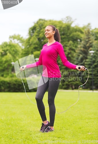 Image of smiling woman exercising with jump-rope outdoors