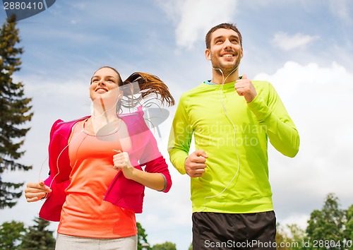 Image of smiling couple with earphones running outdoors