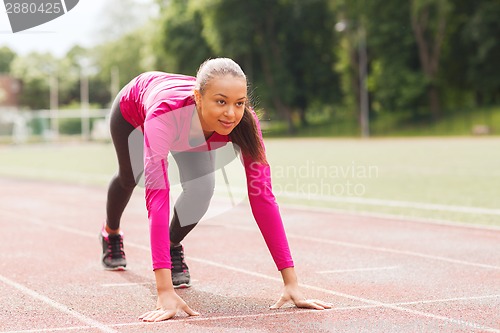 Image of smiling young woman running on track outdoors